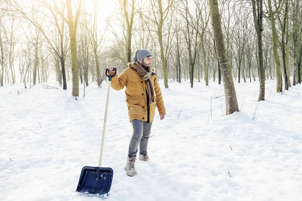 Ung man skotta snö nära en liten trä — Stockfoto