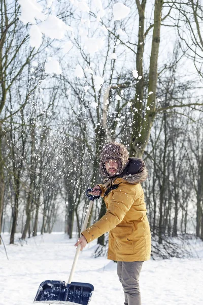 Ung man skotta snö nära en liten trä — Stockfoto