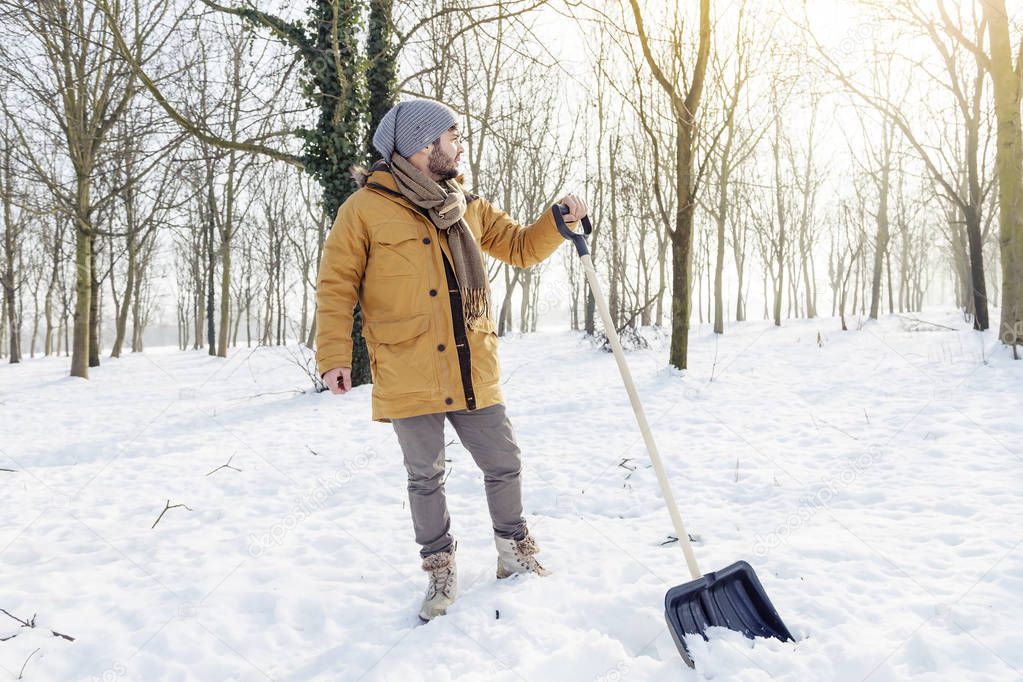 Young man shoveling snow near a small wood — Stock Photo