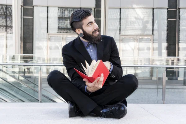 Jovem hipster lendo um livro sentado ao ar livre — Fotografia de Stock