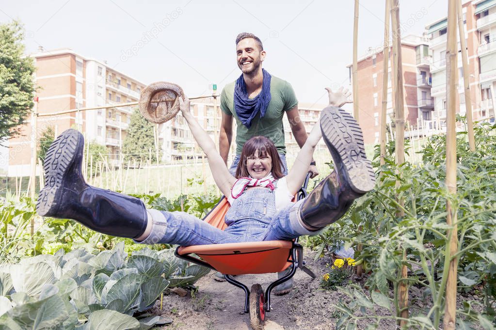 man pushes his girlfriend in wheelbarrow in the garden