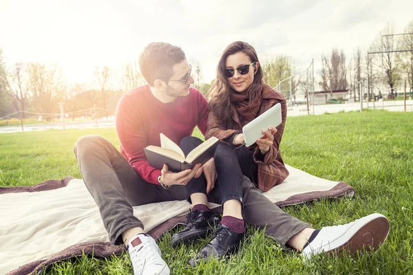 Mooi paar vriendjes ontspannen op weide kijken boek en sm — Stockfoto