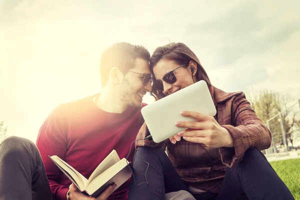 Agradable pareja novios relajarse en prado mirando libro y sm —  Fotos de Stock