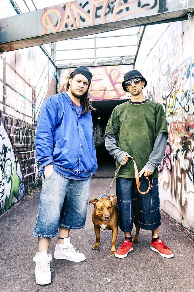 two rap singers with a dog in a subway with graffiti in the back