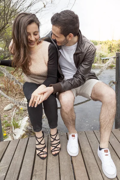 Nice couple of boyfriends embraces and kisses on a wooden bridge — Stock Photo, Image