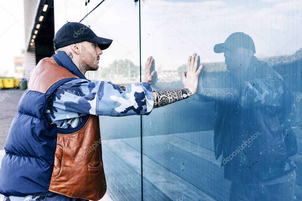 a rap singer is reflected in a blue mirror on the outskirts
