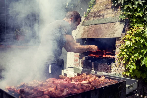 Hombre guapo preparando carne a la parrilla para amigos al aire libre — Foto de Stock