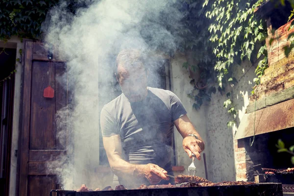 Hombre guapo preparando carne a la parrilla para amigos al aire libre — Foto de Stock