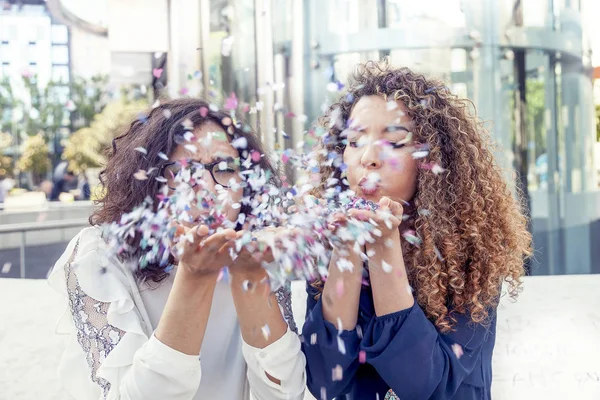 Dwie dziewczyny wieje jakiś kawałek konfetti — Zdjęcie stockowe