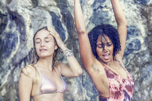 Zwei hinreißende Mädchen spielen einander unter einem kleinen Wasserfall — Stockfoto