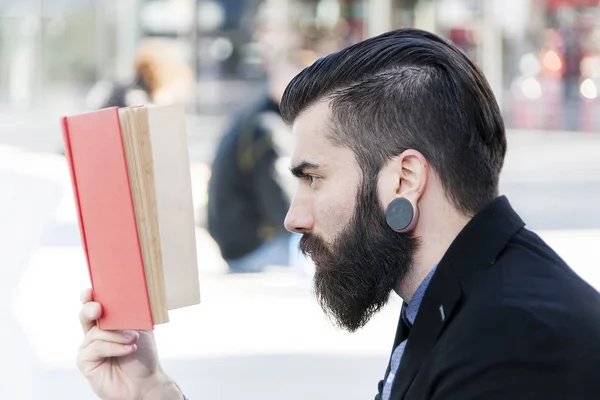 Jovem hipster lendo um livro sentado ao ar livre — Fotografia de Stock