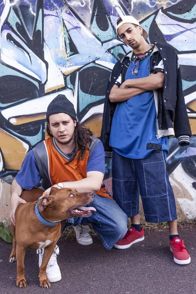 Two rap singers with a dog in a subway with graffiti in the back — Stock Photo, Image