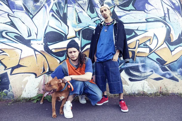 Deux chanteurs de rap avec un chien dans un métro avec des graffitis à l'arrière — Photo