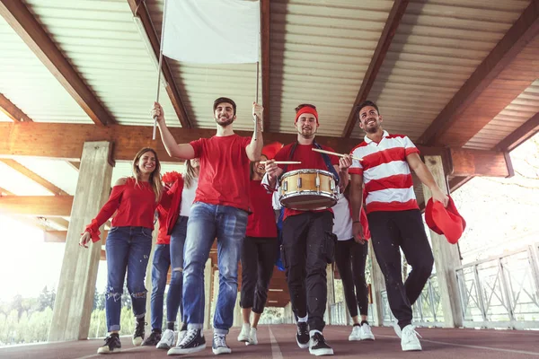 Grupo de fãs vestidos de cor vermelha andando sob o telhado — Fotografia de Stock