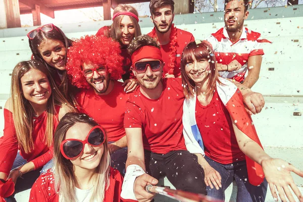 Grupa fanów ubrany w czerwony kolor ma selfie w podstawce — Zdjęcie stockowe