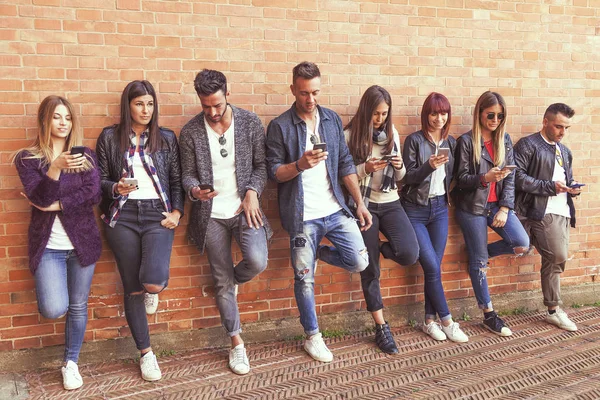 Grande grupo de amigos usando telefone inteligente contra uma parede vermelha — Fotografia de Stock