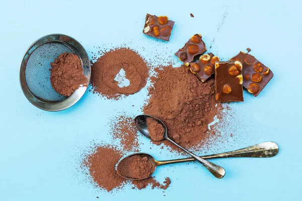 Cacau em pó e pedaços de chocolate em um fundo azul claro — Fotografia de Stock