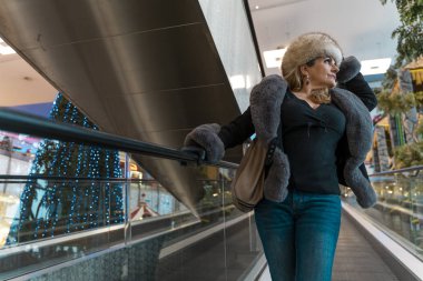 Çekici bir kadın bir departmanda yürüyen merdivenlerden iniyor.