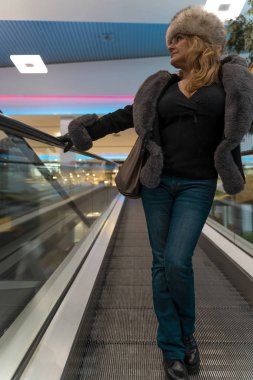 Çekici bir kadın bir departmanda yürüyen merdivenlerden iniyor.