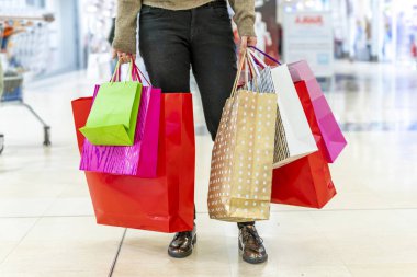 Kadın alışveriş merkezinde renkli alışveriş torbaları gösteriyor.