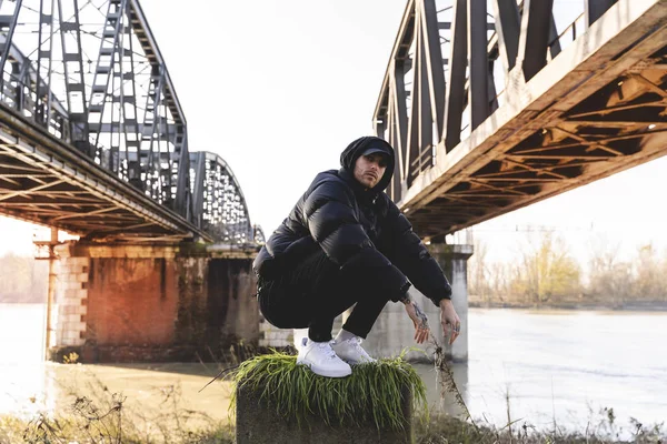 Portrét mladého rappera pózujícího pod kovovým mostem — Stock fotografie