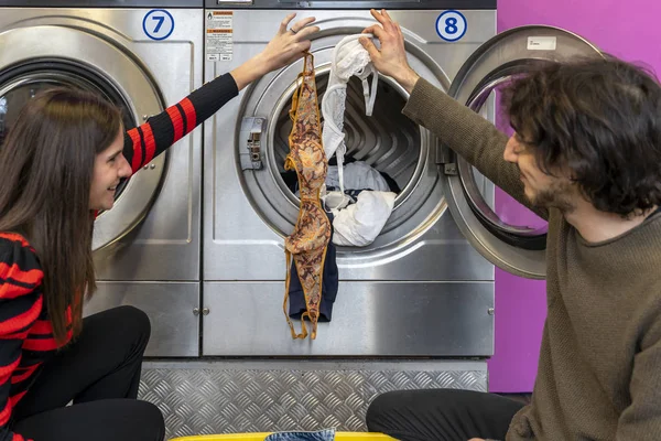 Молодая пара кладет одежду в барабан стиральной машины — стоковое фото