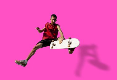 Genç kaykaycı pembe bir arka planda tek başına tahtayla zıplıyor.