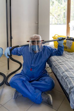 Koruyucu giysili bekar adam elektrikli süpürgeyle evi temizliyor.