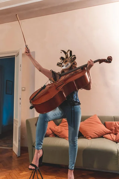 attractive woman wearing a mask is playing a cello indoors