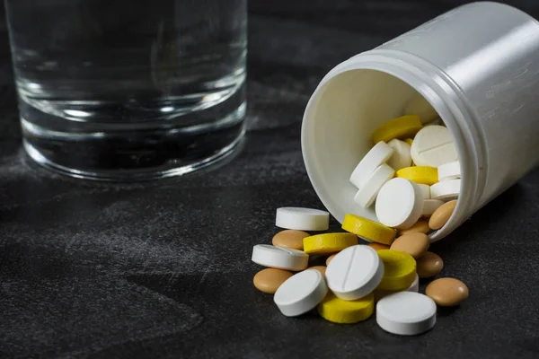 Bir bardak su ile siyah bir tabloda hapları yığını