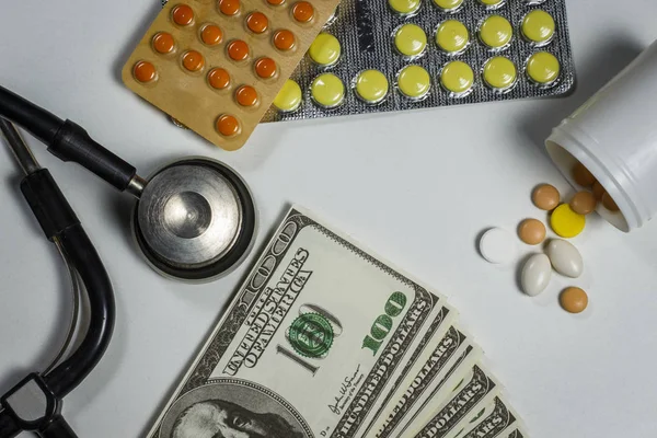 Un montón de pastillas, un estetoscopio y dinero en una mesa blanca — Foto de Stock