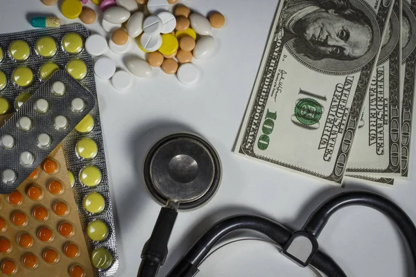 Un montón de pastillas, un estetoscopio y dinero en una mesa blanca — Foto de Stock