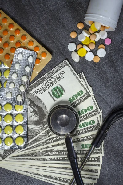 Un montón de pastillas, un estetoscopio y dinero en una mesa oscura — Foto de Stock