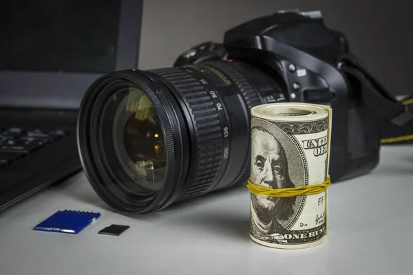 Spoustu dolarů poblíž kamera a notebook — Stock fotografie