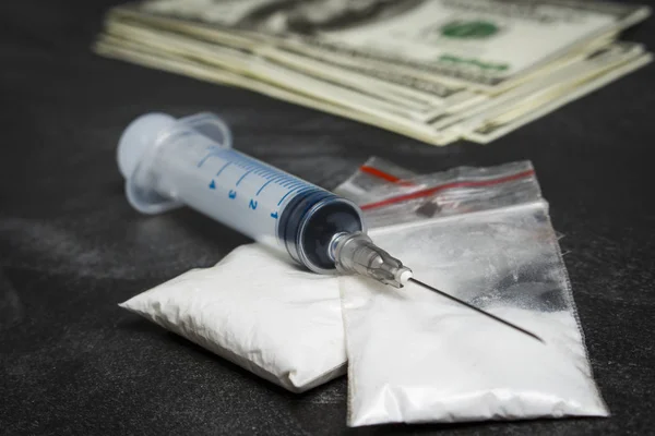 Jeringa y bolsas de plástico con drogas cerca de una pila de dólares — Foto de Stock