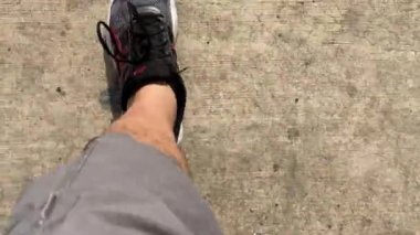 Sokakta şort ve spor ayakkabı giymiş bir adamın bacaklarının en üst görüntüsü.