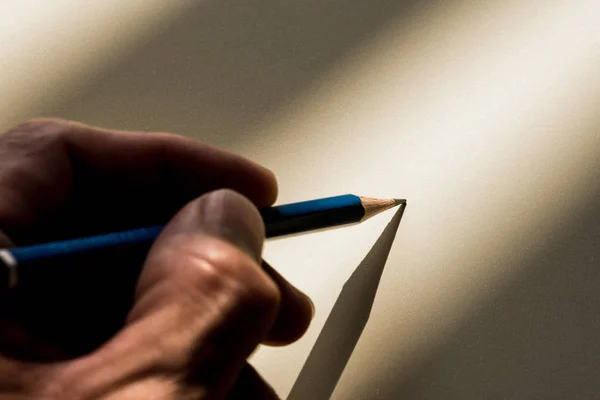 Человеческая рука держит карандаш, чтобы писать на бумаге в тени — стоковое фото