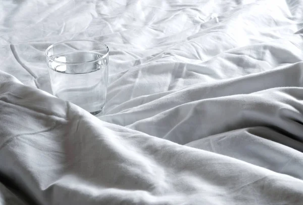 Verre d'eau sur la couverture froissé sur le lit — Photo