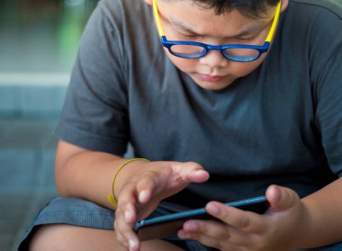 Asyalı çocuğun akıllı telefondan oyun oynarken ciddi bir yüzü var.