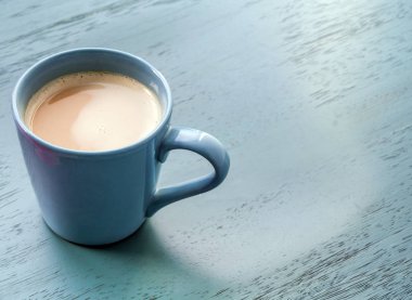 Pastel mavi ahşap zemin üzerinde mavi bir fincan kahve süt