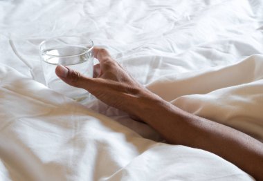 Yatakta su bardağını tutan el.