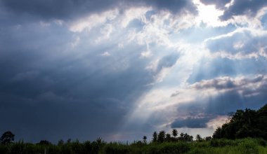 Kırsaldaki kara bulutların arkasındaki güneş ışığı huzmesi.