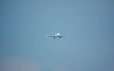 İniş yapan bir uçak mavi gökyüzü sırt deliğiyle bir havaalanına yaklaşıyor.