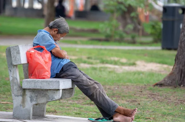 Old man sitting and sleeping on a stone chair in a park in Chang