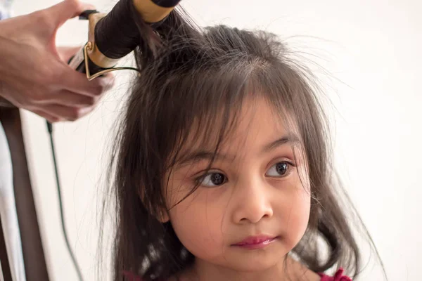 Stylist curling hair for little girl in a parlor