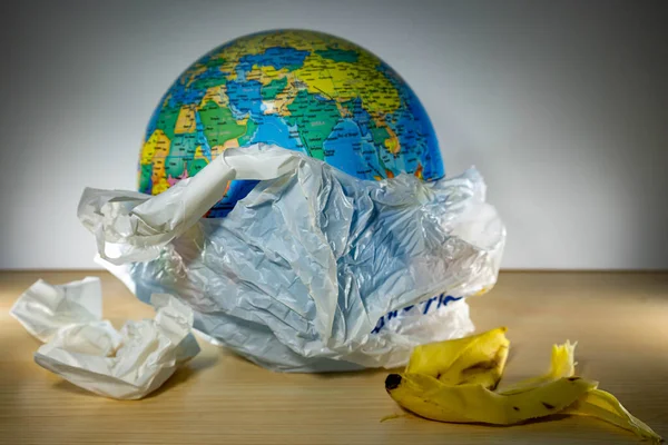Earth inside a plastic and some garbage like paper and banana leftovers. Earth is being destroyed because of too much plastic