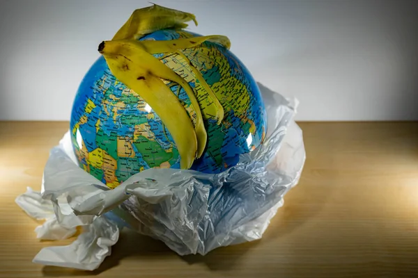 Earth inside a plastic and some garbage like paper and banana leftovers on top of the globe. Earth is being destroyed because of too much plastic