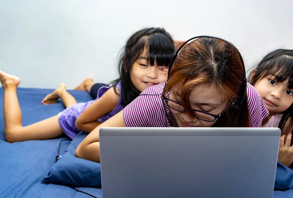 一个带着笔记本电脑和耳机在家里床上工作的女孩被孩子们打扰了 在家里工作的妈妈在接到通知后在家工作 因为爆发了病毒 — 图库照片