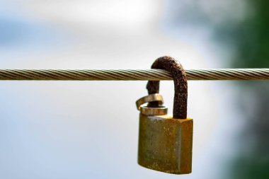 Metal bir kabloda asılı olan paslı asma kilit evlilik ve aşkı simgeliyor.