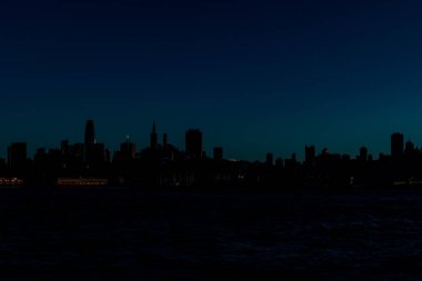 Karanlık siluet manzaralı binalar ve mavi gece gökyüzü şekilli bir şehir.